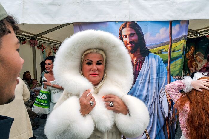 Woman in white fur coat posing inside a tent with a religious backdrop, capturing life on the margins of modern Ireland.