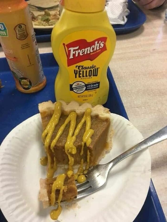 Slice of pie with mustard drizzled on top on a paper plate, next to a bottle of classic yellow mustard.