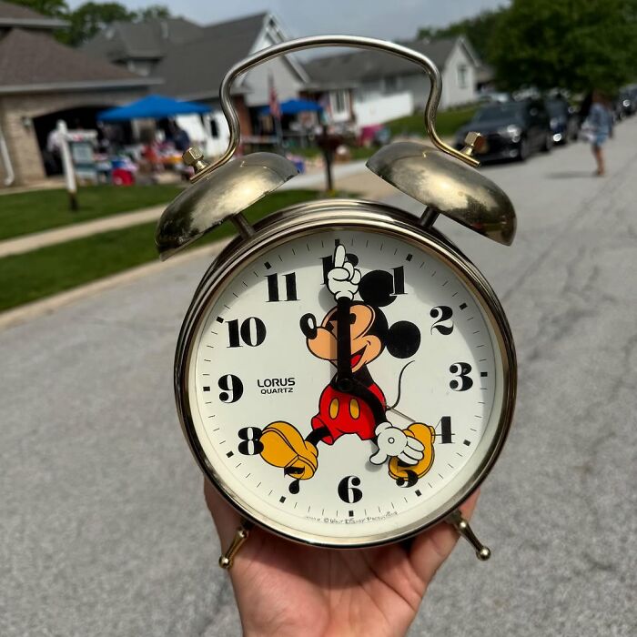 Vintage Mickey Mouse alarm clock held outdoors on a street, a cool secondhand find in a suburban neighborhood setting.