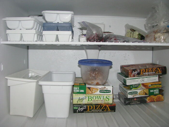 Organized freezer with everyday items under $300 including frozen pizzas, bowls, and ice cube trays for improved convenience.