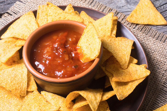 Bowl of salsa surrounded by yellow corn tortilla chips, illustrating cultural food habits and dining differences.