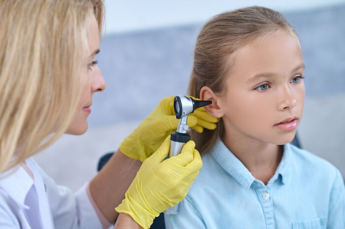 Female doctor wearing yellow gloves examining a young girl's ear during a medical checkup about dismissive doctors.