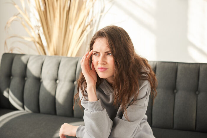 Young woman in casual wear sitting on a couch, showing signs of contemplation reflecting childhood struggles.