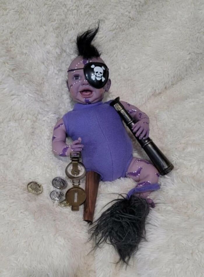 Baby doll dressed as a pirate with an eyepatch, mohawk, and toy accessories, showing a DIY craft shaming project fail.
