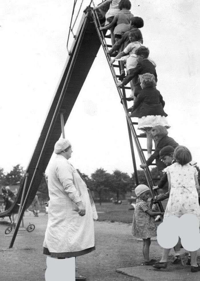 Children climbing a tall slide ladder under adult supervision in a fascinating historical photo from the past.