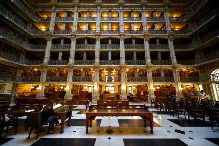 Grandiose library interior with ornate balconies, filled with books and warm lighting, showcasing a magical reading space.