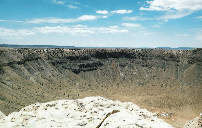Wide view of a rocky meteor crater under a blue sky, illustrating intriguing and bizarre astronaut facts about space exploration.