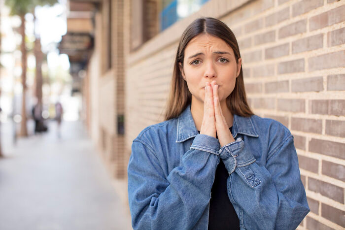 Young woman with worried expression and hands clasped, illustrating signs of a difficult childhood experience outdoors.