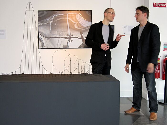 Two men discussing a wire sculpture in a gallery setting, evoking themes of scary and unsettling Wikipedia articles.