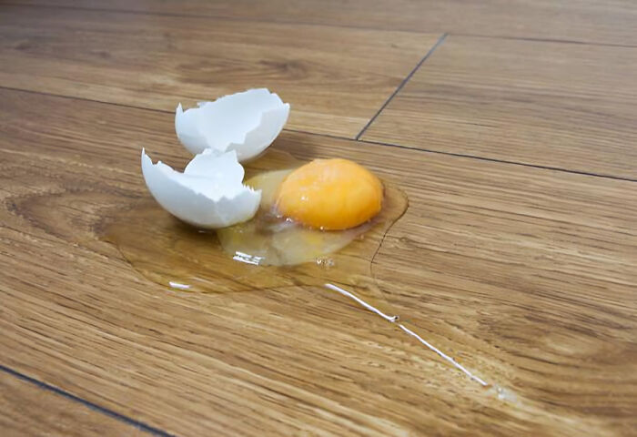 Broken egg with yolk spilled on wooden floor, symbolizing unresolved personal mysteries people doubt they'll ever solve.