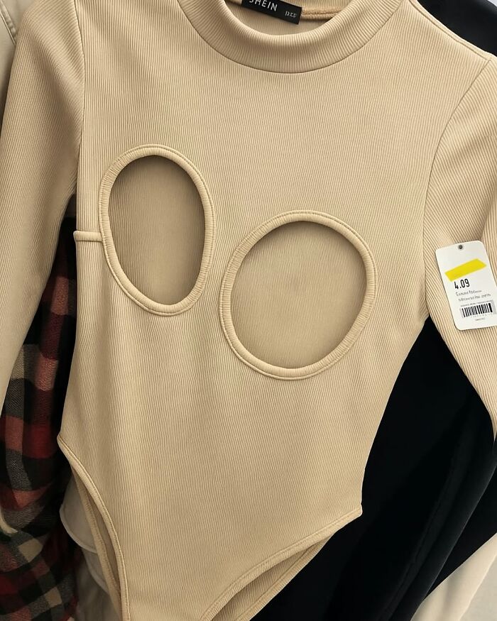 Beige ribbed secondhand bodysuit with two large circular cutouts on chest, hanging in thrift store among other clothes.