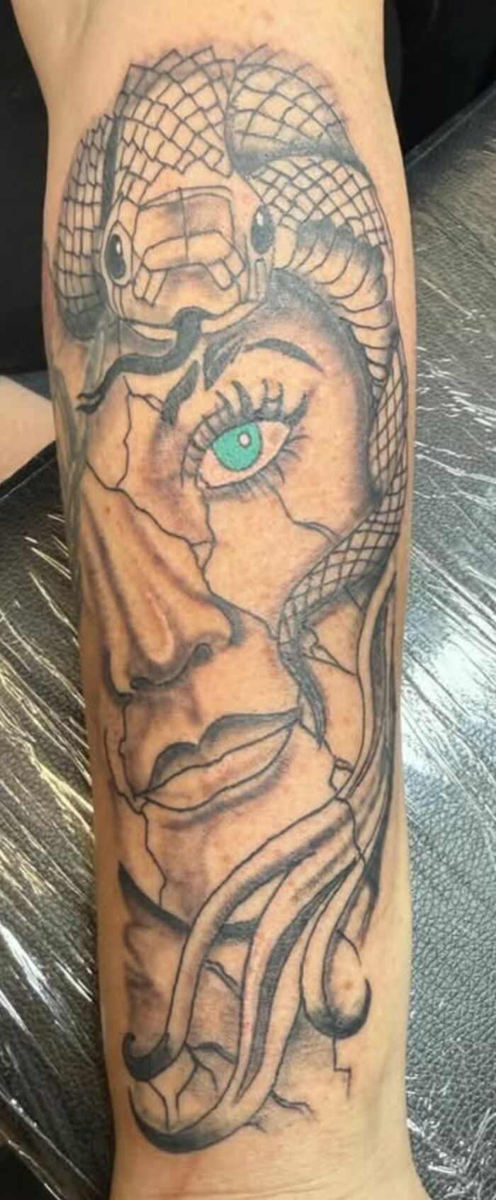 Tattoo of a broken c*****d face with a snake wrapped around it and an eye colored teal, showcasing bad tattoos.