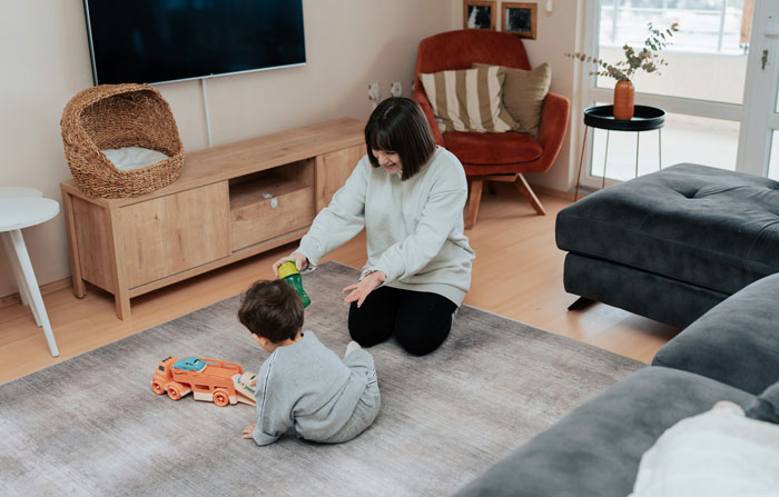 Woman babysitting child at home playing with toys on a rug, highlighting unpaid babysitting by a colleague on their day off Woman babysitting child at home playing with toys on a rug, highlighting unpaid babysitting by a colleague on their day off