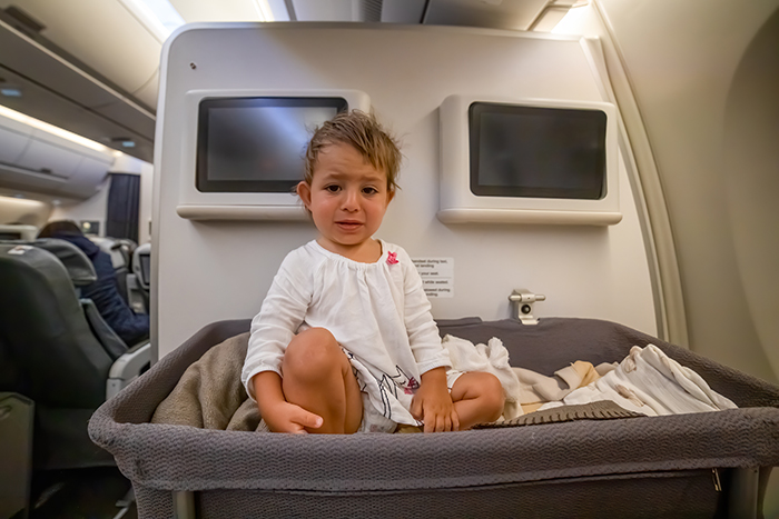 Toddler sitting in airplane bassinet looking upset during a flight, relating to rebooking to avoid babysitting niece. Toddler sitting in airplane bassinet looking upset during a flight, relating to rebooking to avoid babysitting niece.