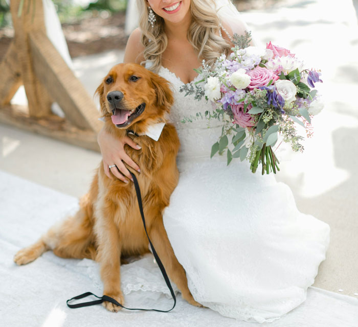 Bride with her pet dog at wedding, replacing kids with pets, holding a bouquet of flowers outdoors.