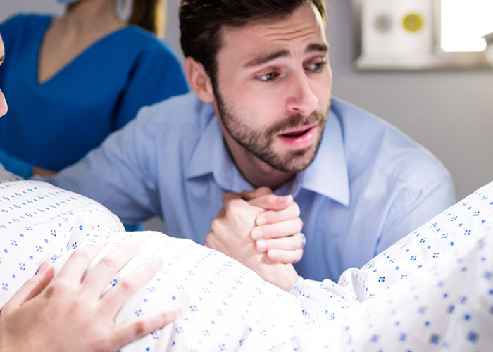 A nervous dad holding his partner’s hand inside the birthing room experiencing childbirth for the first time.