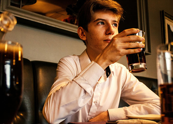 Young man sitting awkwardly at a restaurant table holding a drink, capturing an awkward date moment from painful dates.