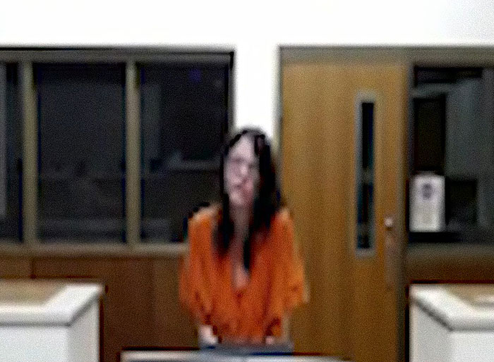 Woman in orange prison uniform standing in courtroom, related to raging mom who drove pickup truck through kids park incident.