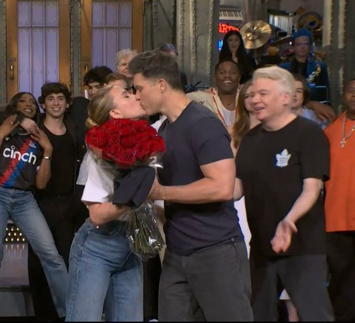Scarlett Johansson kissing costar on the lips at premiere, holding red roses, surrounded by smiling cast members.