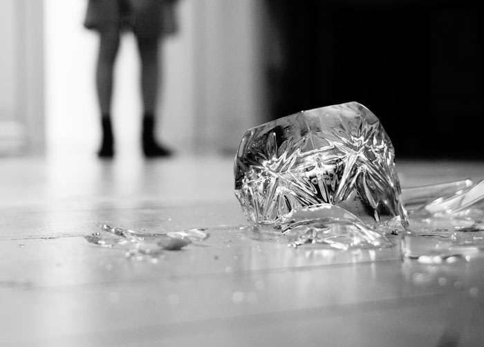 Broken glass on the floor with a blurred figure in the background illustrating surprising effective old wives tales safety tips.