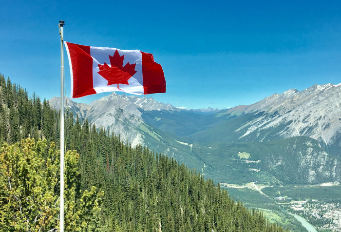 Canadian flag waving over mountain landscape, symbolizing one of the best countries to live in 2025 rankings.