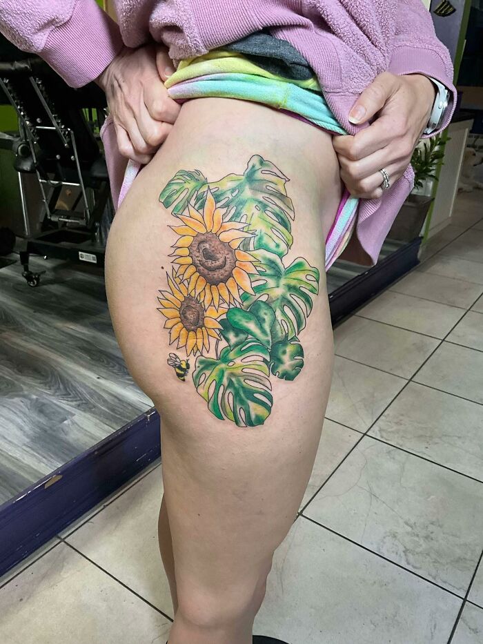 Colorful sunflower and monstera leaf tattoo on thigh, showcasing a vibrant botanical design, part of hilariously bad tattoos collection.