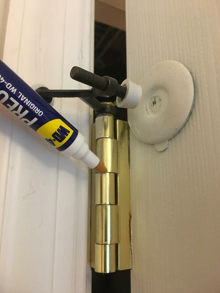 Close-up of a door hinge being marked with a WD-40 marker, demonstrating a simple fix for common household glitches.