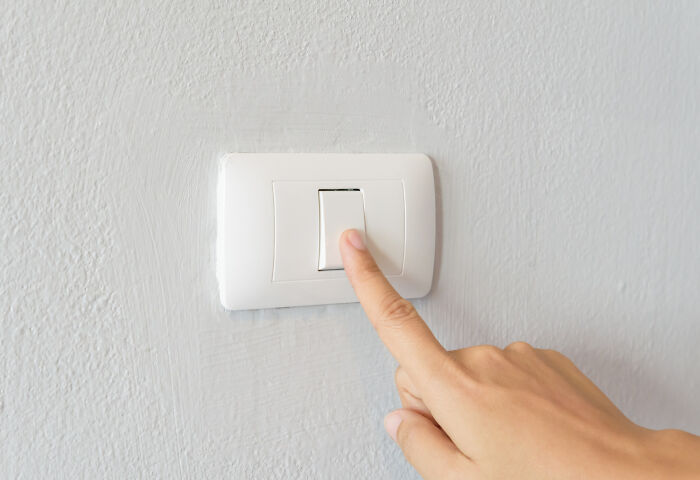 Hand pressing a white light switch on a textured gray wall illustrating poor people habits concept.