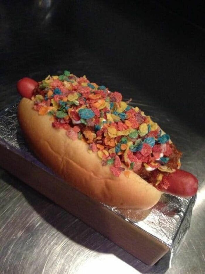 Hot dog topped with colorful cereal flakes, an unusual cursed picture of food that might make you go eeeeuw.