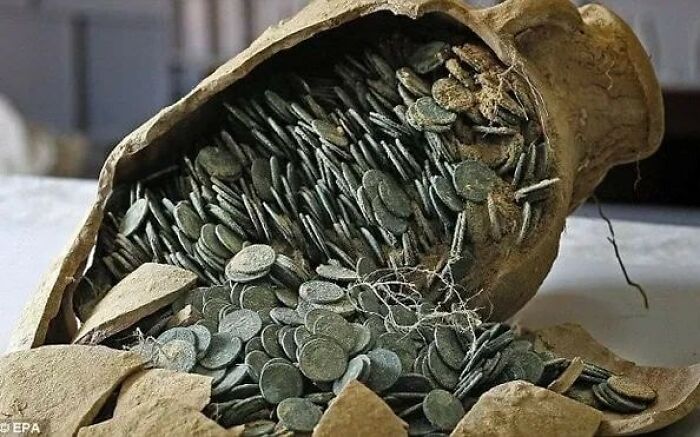 Ancient pottery jar filled with numerous old coins discovered in an archaeology world excavation site.