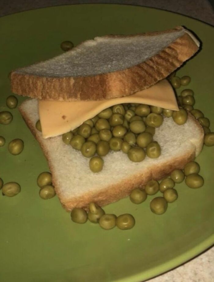 Sandwich with cheese slice and loose peas on white bread on a green plate, a cursed food picture example.