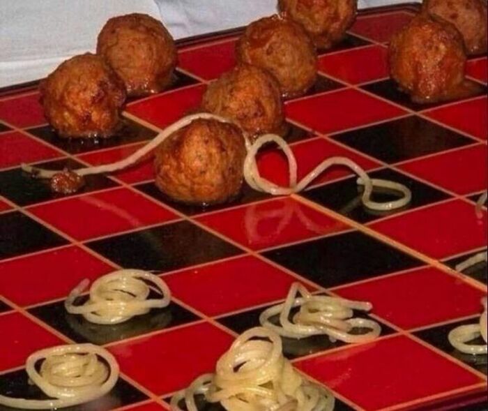 Red and black board with meatballs and spaghetti arranged like a chess game in cursed food pictures.