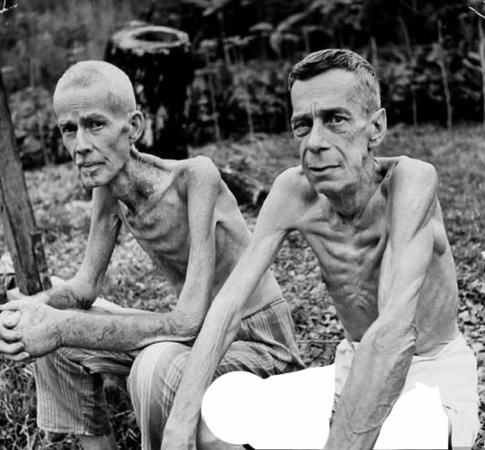Two extremely emaciated men sitting outdoors, a striking historical photo revealing harsh past realities.