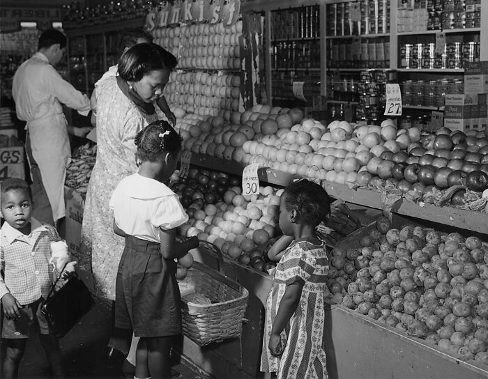 1940s housewife shopping with children at a fruit and vegetable market, showcasing daily life moments.