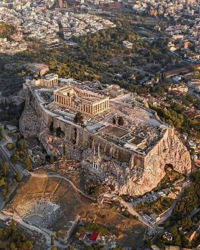 Aerial view of ancient archaeological site with historic ruins atop a rocky hill surrounded by modern cityscape in archaeology world.