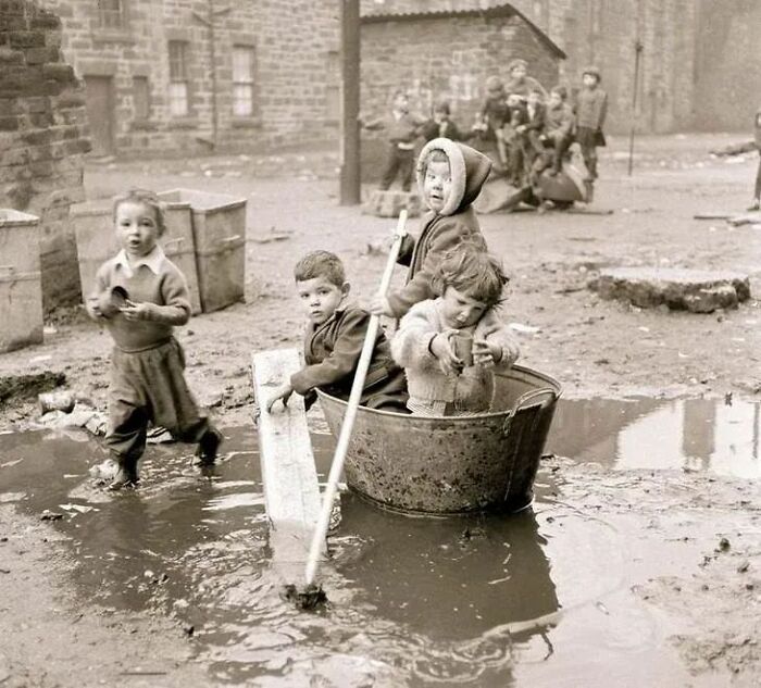 Children playing in a muddy area with makeshift boats, a fascinating historical photo showing life in the past.
