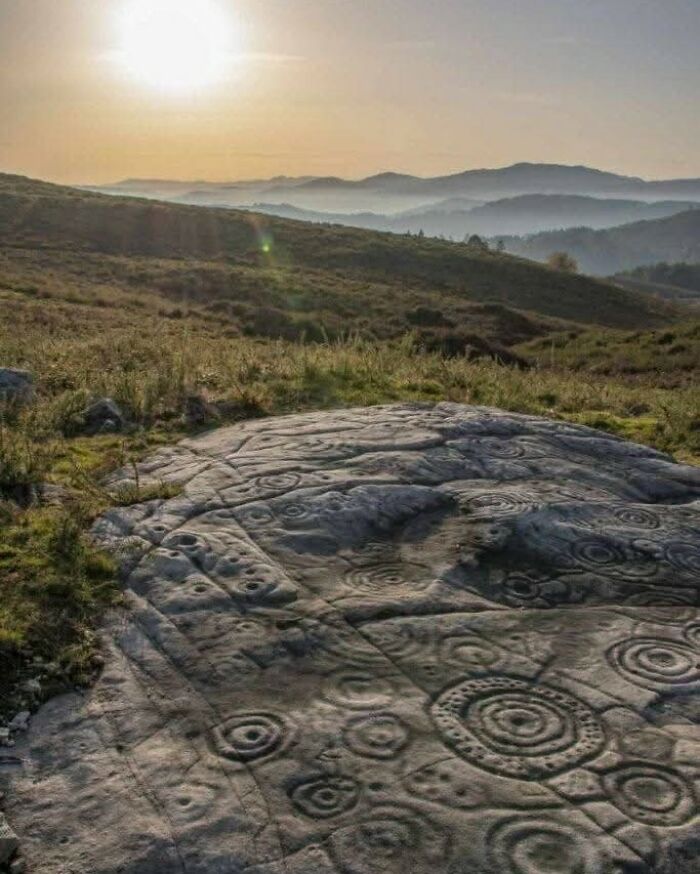 Ancient carved stone with spiral patterns in a grassy landscape at sunset, showcasing archaeology world historical significance.