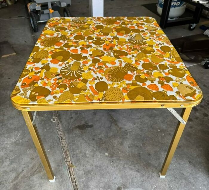 Vintage secondhand table with retro mushroom pattern and foldable metal legs in a garage setting.