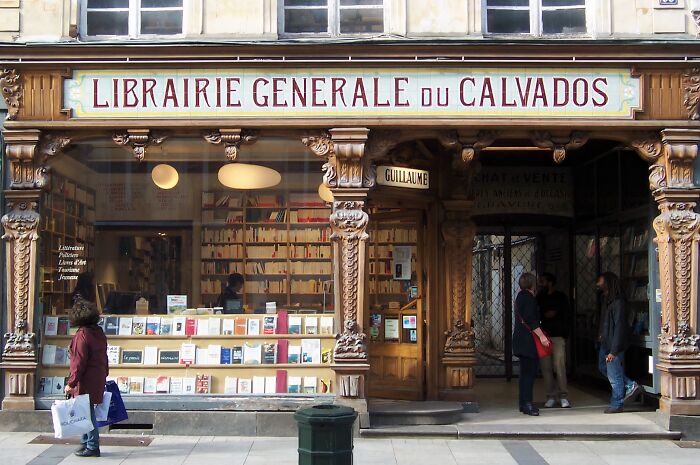 Exterior of a grandiose and magical bookstore with wooden carvings and books displayed in the window from around the world.