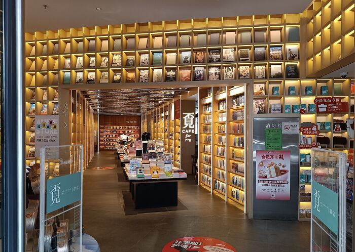 Modern library interior with warm lighting, wooden shelves, and a cozy atmosphere featuring numerous books and reading spaces.