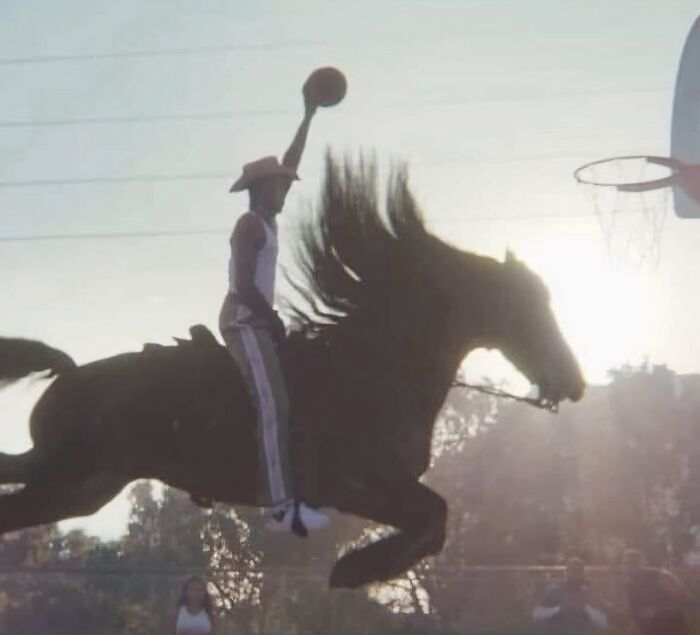 Hombre en un caballo saltando mientras sostiene un balón cerca de un aro de baloncesto en una imagen maldita.