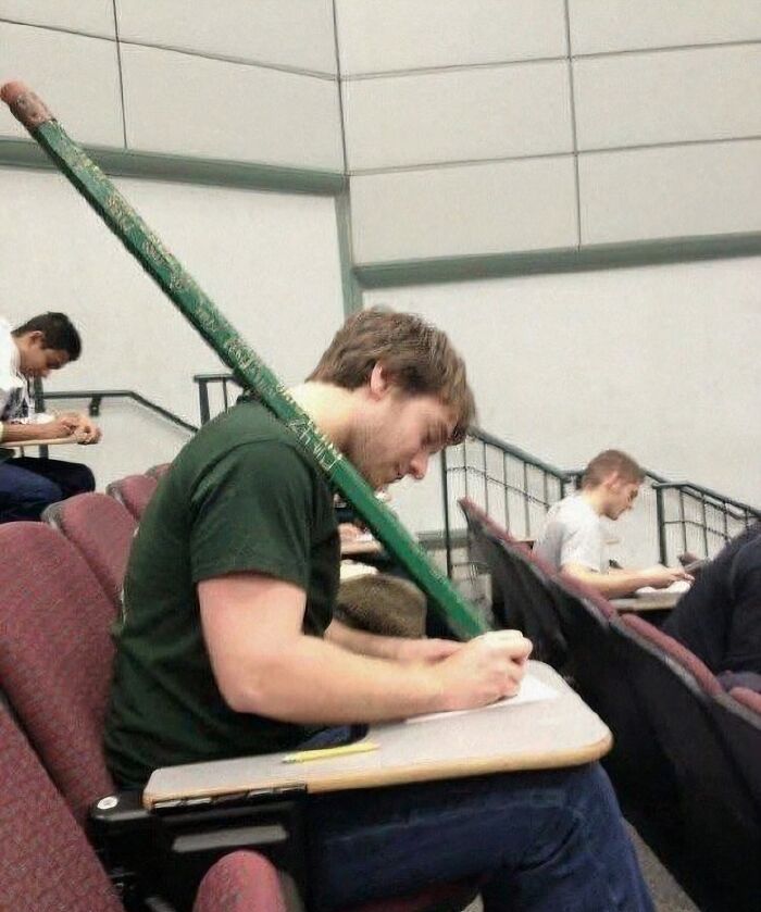 Joven usando un lápiz gigante para escribir en un salón de clases, imagen maldita a todos los niveles.