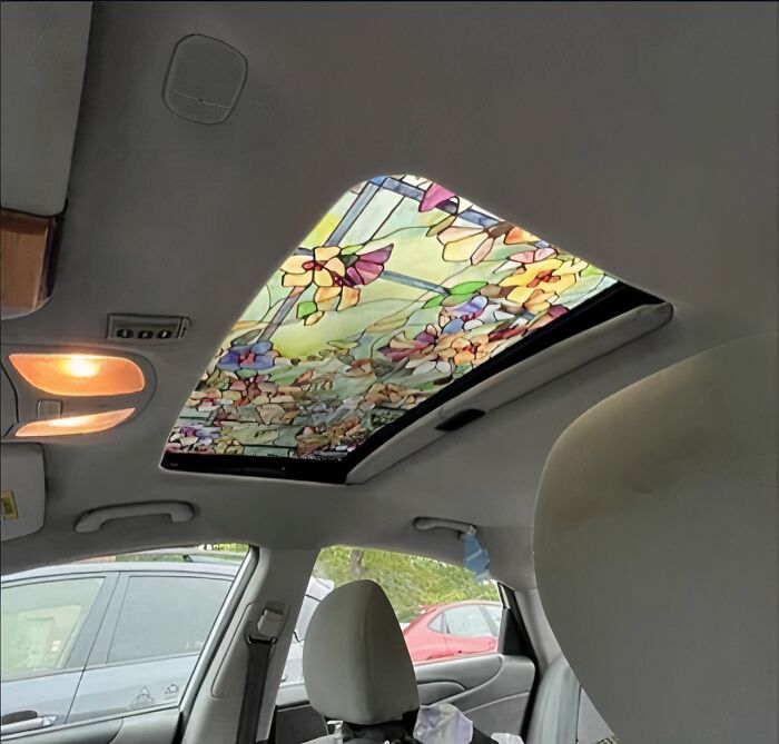 Interior de coche con techo solar cubierto por imagen maldita de vidrieras decorativas coloridas.
