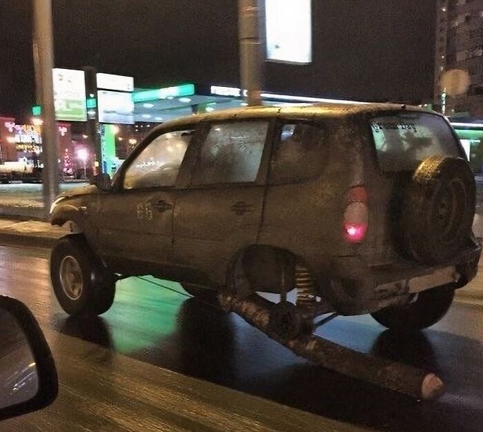 Auto maldito sin ruedas traseras circulando de noche en calle iluminada, imagen sorprendente y peligrosa.
