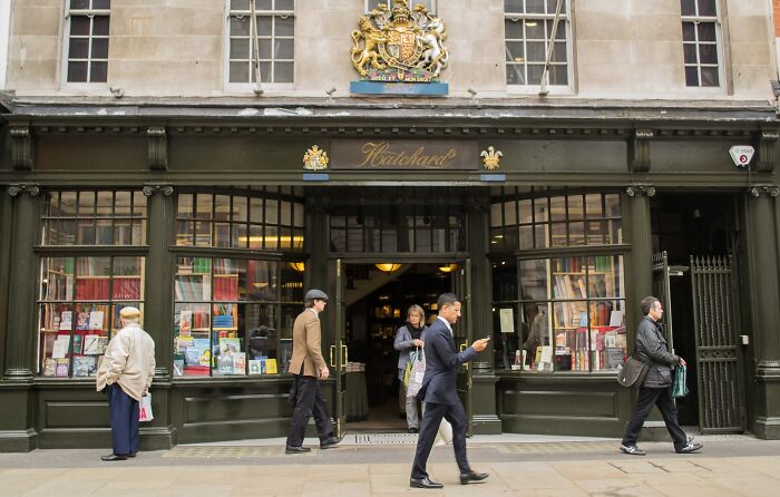 Exterior view of a stunning and impressive bookstore with large display windows and people walking by on the street.