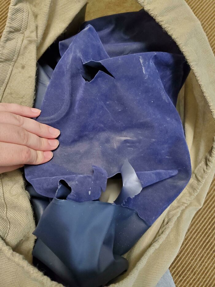 Hand holding a torn and damaged inflatable object inside a beige fabric container showing people damaging things they borrowed.