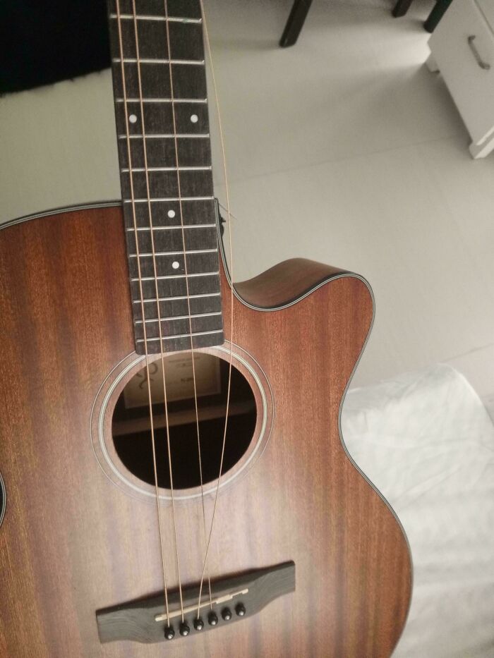 Acoustic guitar with broken and loose strings showing damage from people borrowing and mishandling it.