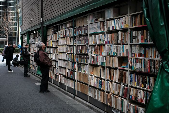 People browsing an outdoor library wall filled with books in a cozy and grandiose library setting from around the world