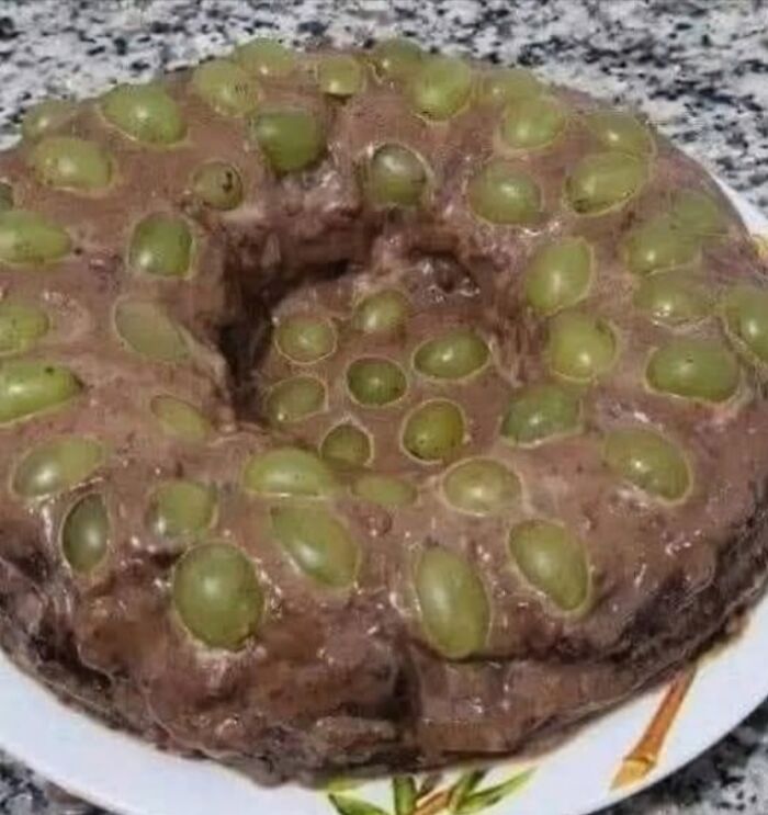 Chocolate cake covered in green grapes with a gooey texture, one of the disgusting food pics to ruin appetite.