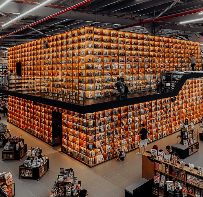 Modern bookstore with illuminated shelves and visitors exploring books in a grandiose and magical library setting.